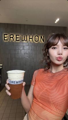 a woman holding up a cup of coffee in front of a sign with the name erewhon on it