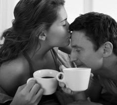 a man and woman kissing while holding coffee mugs