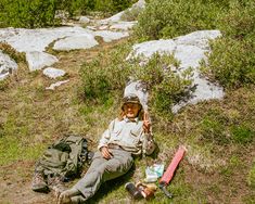 a man laying on the ground next to a backpack and camping gear in front of some rocks