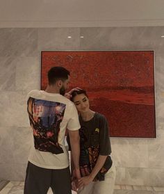 two people standing next to each other in front of a painting