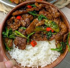 someone is holding a bowl full of rice and beef with peppers on top, next to another bowl filled with white rice