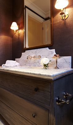 a bathroom with a marble counter top and wooden drawers, along with two lights on either side of the vanity