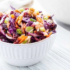 a white bowl filled with coleslaw salad on top of a wooden table next to a napkin