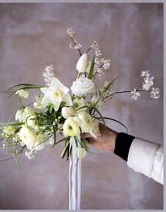 a person holding a bouquet of white flowers in their left hand and the other hand reaching for it