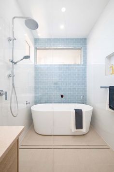 a white bath tub sitting next to a window in a bathroom with blue tiles on the walls