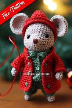 a small crocheted mouse wearing a red coat and green shirt, standing next to a christmas tree