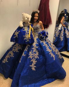 a woman in a blue and gold dress holding a teddy bear next to a mirror