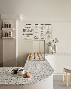 a counter top with donuts on it next to a cup of coffee and two chairs