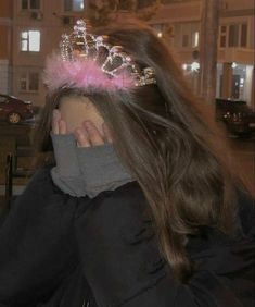 a woman wearing a tiara with pink feathers on her head and covering her face