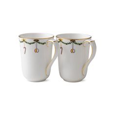 two white coffee cups with gold trimmings and holly decorations on the sides, one is