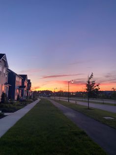 the sun is setting over some houses in an area that has grass and trees on both sides