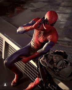 a man in a spiderman costume sitting on a bench next to a bag and backpack