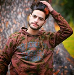 a young man is standing in front of a tree with his hand on his head