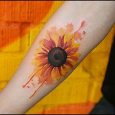 a sunflower tattoo on the arm with watercolor paint splatters all over it