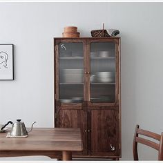 a wooden table sitting next to a tall cabinet with glass doors on it's sides