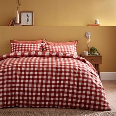 a red and white checkered comforter set on a bed in a room with yellow walls