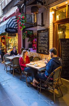 two people sitting at a table in front of a restaurant