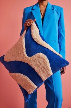 a woman holding a large blue and beige pillow in her hands, with one hand on it