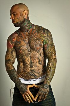 a man with lots of tattoos on his body and chest standing in front of a white wall