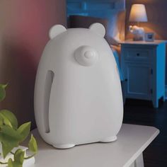 a white bear shaped humider sitting on top of a table next to a plant