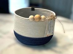 a blue and white woven basket with two small wooden beads on the top, sitting on a table