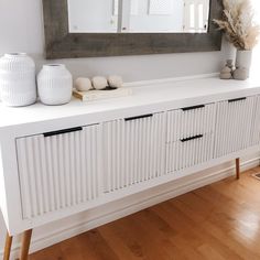 a white sideboard with two vases and a mirror on it's wall