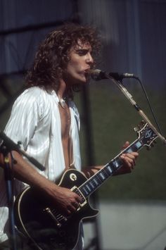 a man with long hair playing an electric guitar in front of a microphone on stage