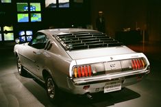 an old mustang muscle car on display in a museum with television screens behind it and people looking at the cars