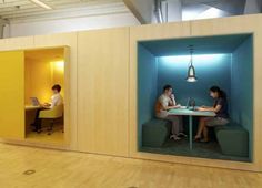 two people sitting at a table in an office cubicle with blue walls and windows