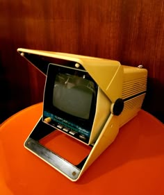 an old fashioned computer sitting on top of a orange table next to a wooden wall