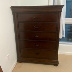 a brown dresser sitting in front of a window next to a white wall and carpet