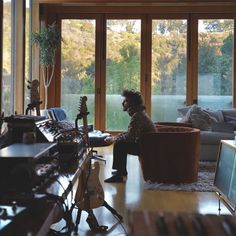 a man sitting in a living room next to a large window with lots of windows