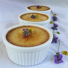 three small white bowls filled with food and flowers on top of a white table cloth