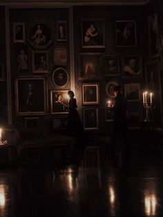 two people standing next to each other in a room with pictures on the wall and candles lit