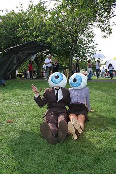 two people sitting in the grass with fake eyes on their heads