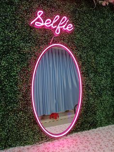 a pink neon sign that says selfie in front of a mirror on a wall