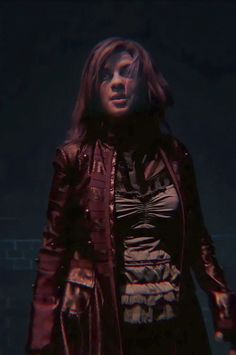 a woman standing in the dark with her hands on her hips and wearing a leather jacket