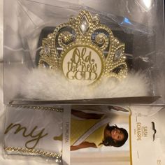 a gold tiara with white feathers in a clear plastic package on a bed sheet