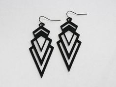 the black and white earrings are hanging from hooks on a white surface, with an intricate geometric design