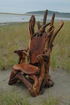 a wooden chair sitting on top of a sandy beach next to grass and water in the background