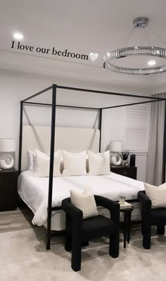 a white bed sitting in a bedroom next to two black chairs and a chandelier