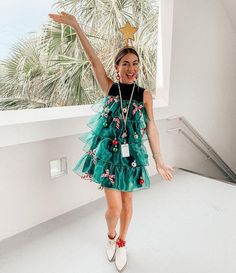 a woman in a green dress is standing by a window with her arms up and smiling