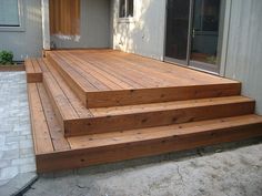 a wooden deck with steps leading up to the front door and patio area behind it