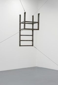 a ladder suspended from the ceiling in an empty room with white walls and grey flooring