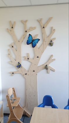 a wooden tree with two blue chairs in front of it and butterflies on the branches