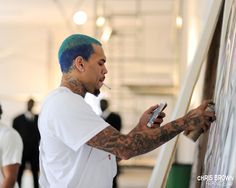 a man with blue hair is writing on a white board and looking at his cell phone