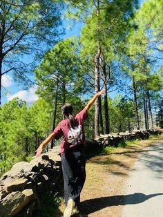 a woman is walking down the road with her arms in the air and trees behind her