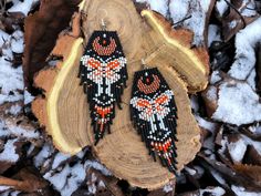 two black and orange beaded bird earrings sitting on top of a piece of wood