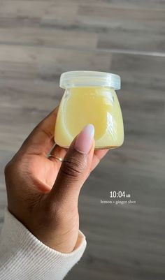 a hand holding a jar of liquid on top of a wooden floor