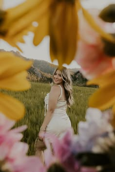 a woman is standing in the middle of flowers with her arms around her chest and smiling